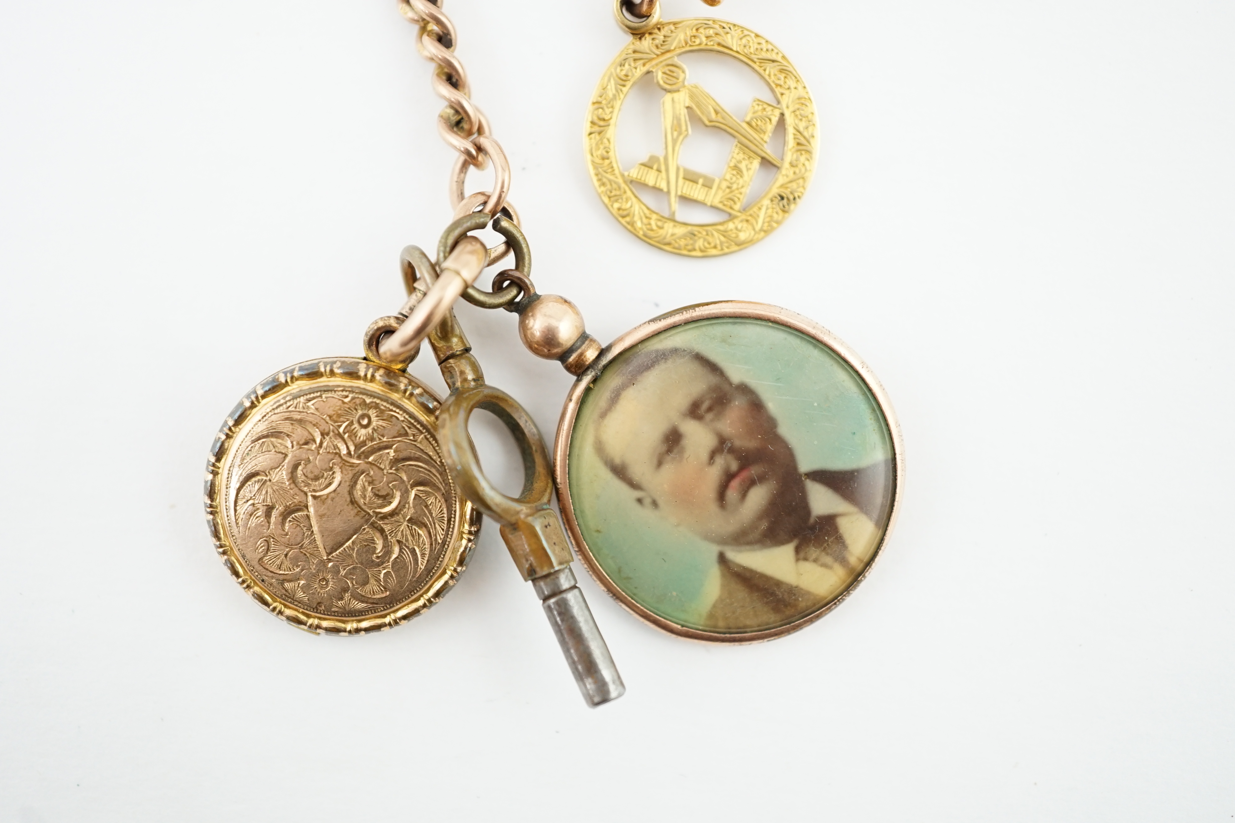 An Edwardian 9ct gold curb link albert, hung with a 9ct gold Masonic charm, locket and a double sided portrait pendant